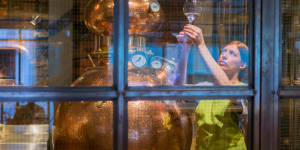 Una joven sonriente junto a un alambique de cobre, mostrando el proceso artesanal de destilación en una micro destilería.